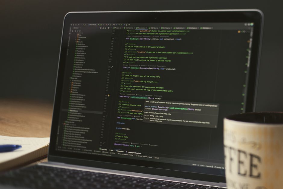 Close-up prikaz laptopa s prikazom programskog koda u prigušenoj prostoriji uz šalicu kave